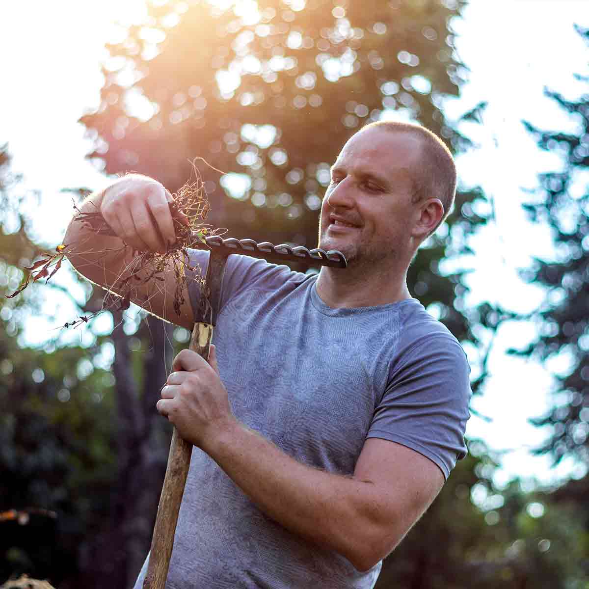 Eastlake Tree Services customer review. Man outdoors holding a garden tool with a spiral drill bit, removing roots and soil in sunlight.